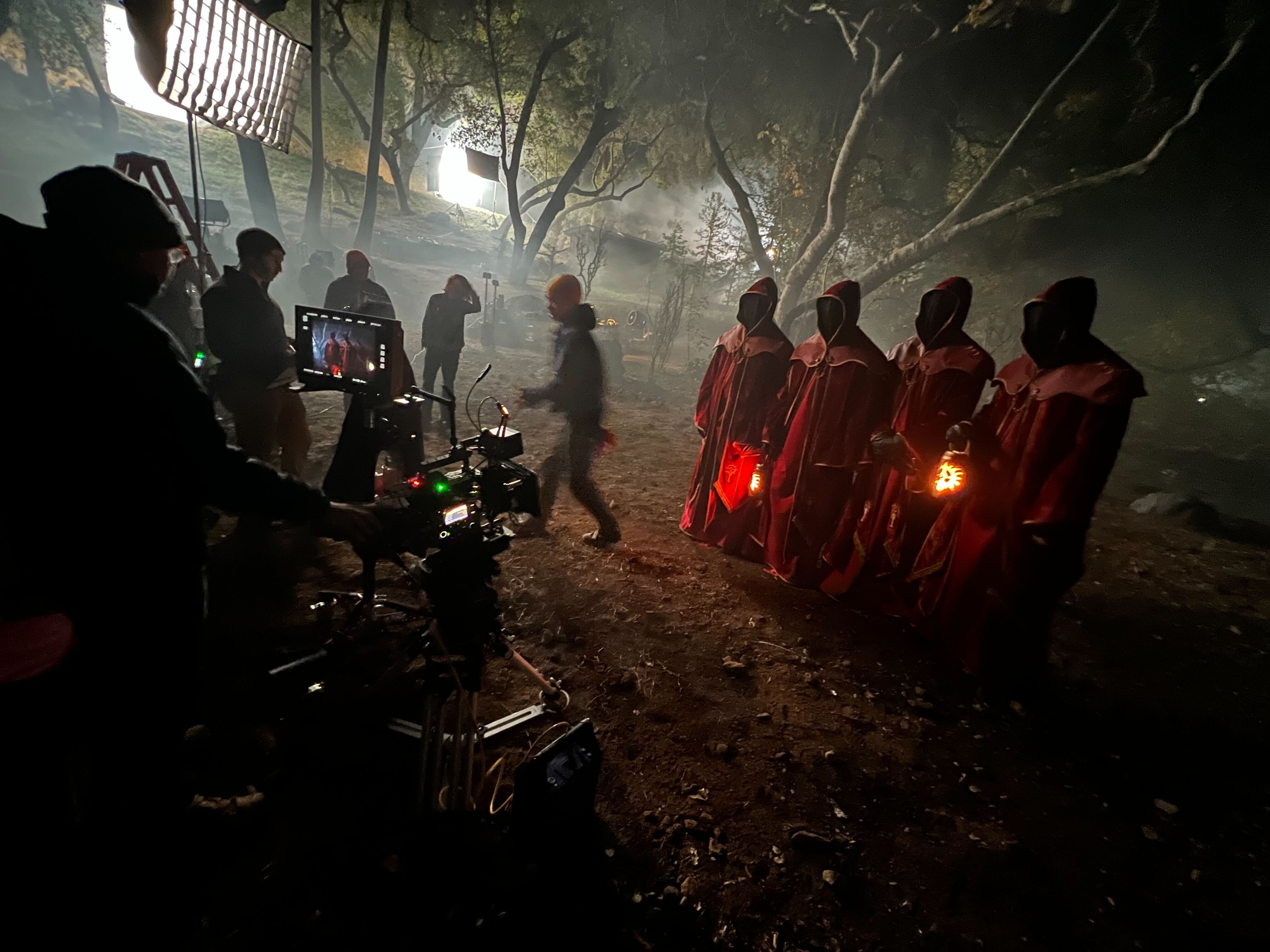 Four hooded Diablo performers on a misty forest set with the camera crew and lighting visible